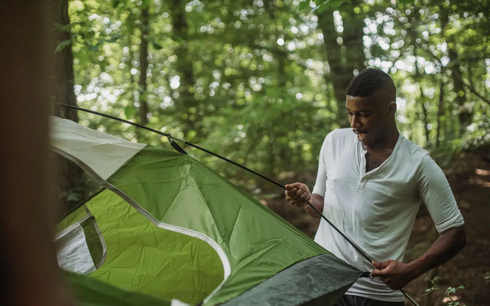 Camper setting up a green dome tent among trees