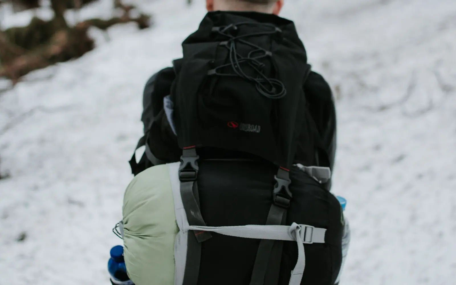 Backpacker on a snowy trail with a sleeping bag strapped to the bottom of a large pack