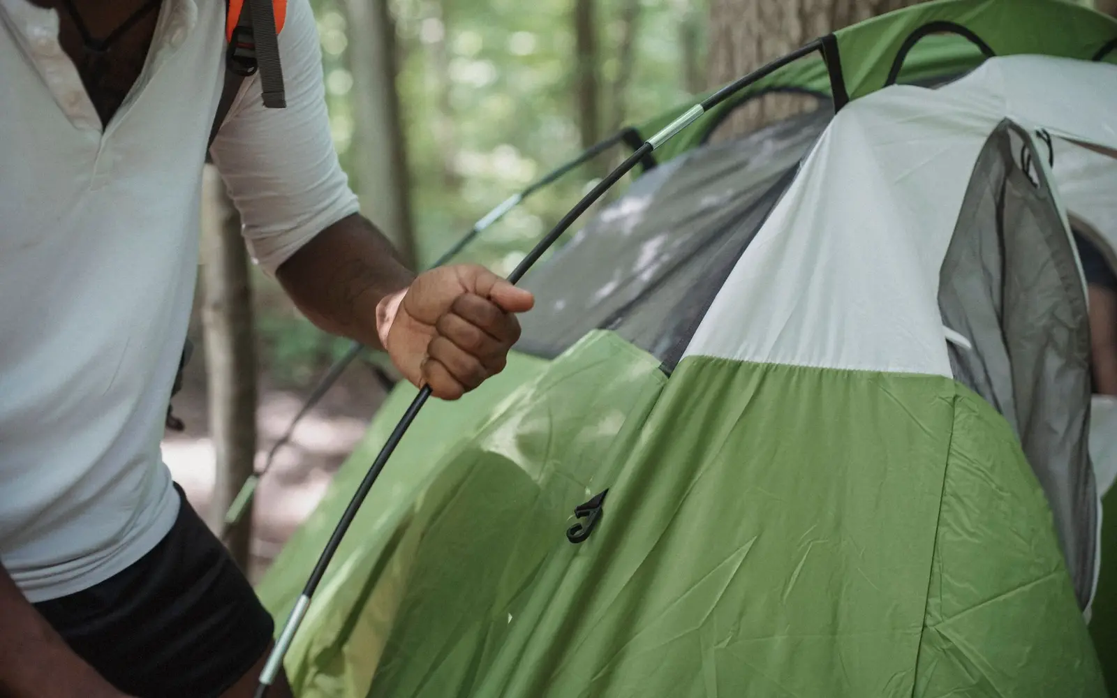 Camper threading a pole through a green dome tent in a leafy forest campsite